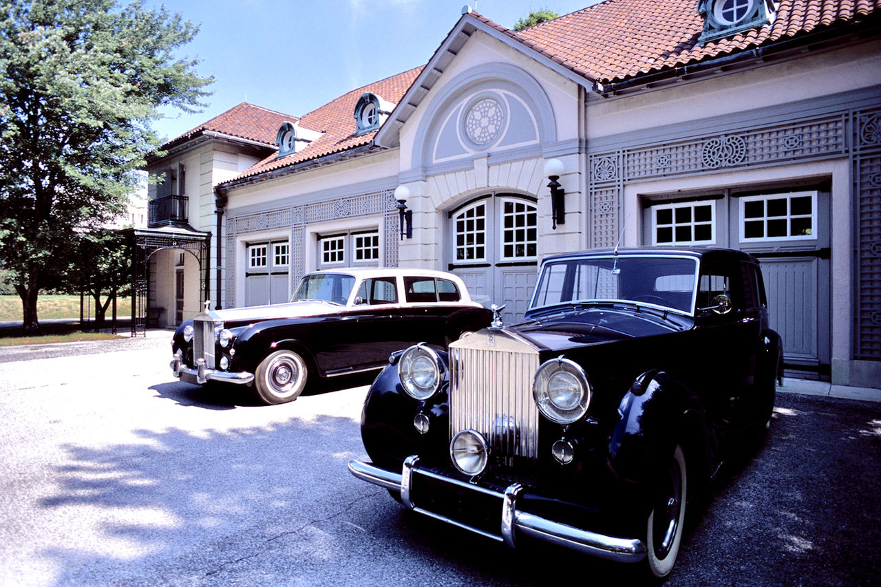 Two classic Rolls-Royce cars are parked outside the Chauffeur's Garage on a sunny afternoon. 